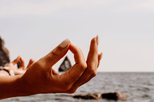 Yoga on the beach. A happy woman meditating in a yoga pose on the beach, surrounded by the ocean and rock mountains, promoting a healthy lifestyle outdoors in nature, and inspiring fitness concept