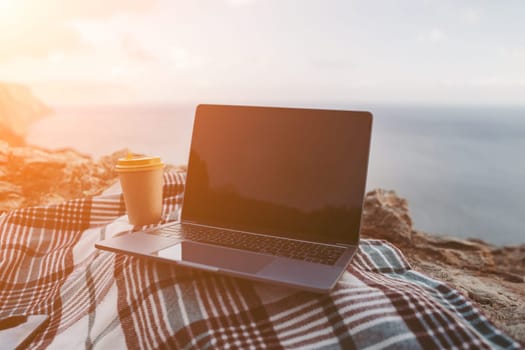 Laptop coffee on blanket with ocean view. Illustrating serene outdoor laptop use. Freelancer enjoying their time outdoors while working or browsing the internet