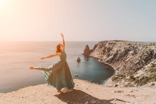 Woman green dress sea. Female dancer posing on a rocky outcrop high above the sea. Girl on the nature on blue sky background. Fashion photo