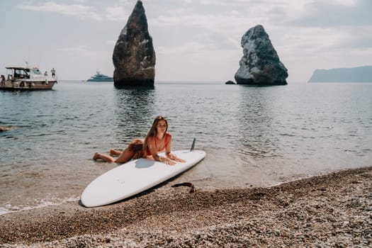 Close up shot of beautiful young caucasian woman with black hair and freckles looking at camera and smiling. Cute woman portrait in a pink bikini posing on a volcanic rock high above the sea