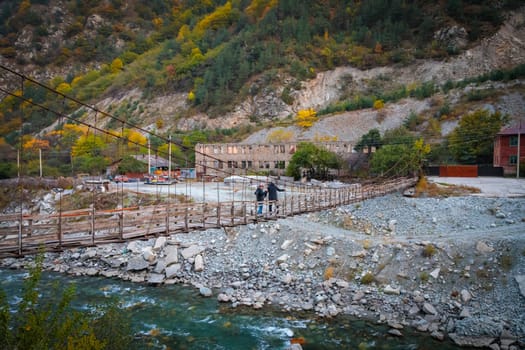 Two men crossing a river on a high suspension bridge while walking