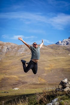 A man happily jumps on the top of a mountain, exhilarating the mesmerizing scenery and his achievement.