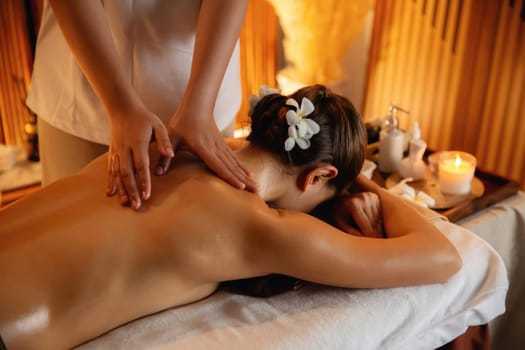 Caucasian woman customer enjoying relaxing anti-stress spa massage and pampering with beauty skin recreation leisure in warm candle lighting ambient salon spa at luxury resort or hotel. Quiescent