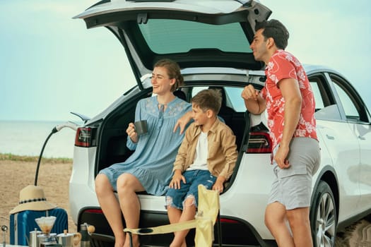 Family vacation trip traveling by the beach with electric car, happy family recharge EV car, enjoying outdoor camping coffee. Seascape travel and eco-friendly car for clean environment. Perpetual