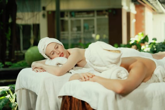 A portrait of a couple of a beautiful young caucasian woman with white towel rest on comfortable spa bed with relaxation while having body massage with professional masseur at spa salon.Tranquility.