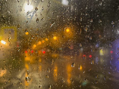 Rain bokeh road lights. Abstract shot of evening city traffic bokeh. Multicolored lights of the evening city and passing cars through a wet rainy window