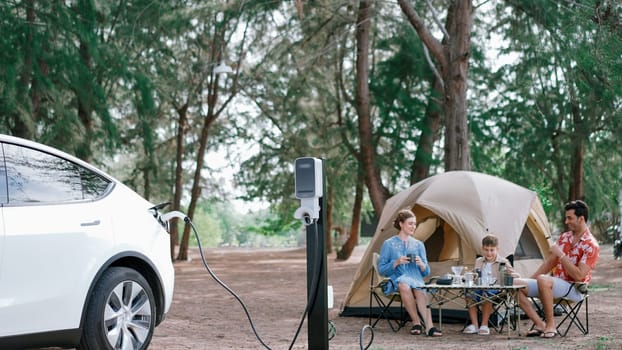 Outdoor adventure and family vacation camping in nature travel by eco friendly car for sustainable future. Lovely family recharge EV car with EV charging station in campsite. Perpetual