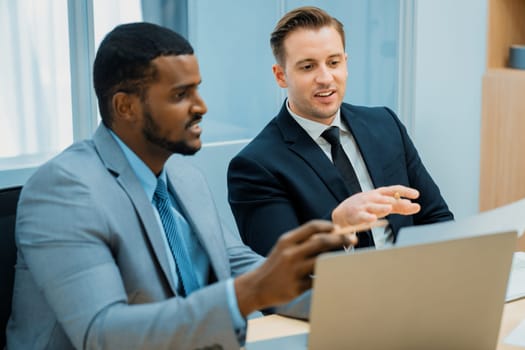 African male leader explain strategy while show solution to professional project manager by pointing at document, using laptop. Skilled business team brainstorming idea. Business meeting. Ornamented.