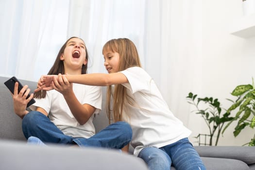Child with smartphone at home. Two kids using smart phone, surfing internet or using social media. Two kids using online mobile phone, call, watching content, playing video games, sitting on couch. High quality photo