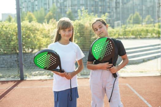 Teenage girls with racquets and balls standing in padel court, looking at camera and smiling. High quality photo