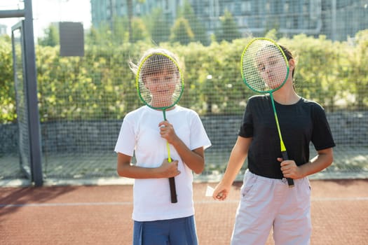 Happy sporty elementary school age girl, child playing badminton, holding a racket making funny faces, portrait, lifestyle. Sports, exercise and healthy outdoor activities leisure concept, one person. High quality photo