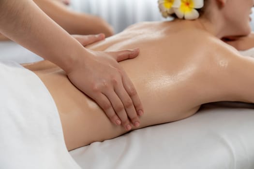 Caucasian couple customer enjoying relaxing anti-stress spa massage and pampering with beauty skin recreation leisure in day light ambient salon spa at luxury resort or hotel. Quiescent