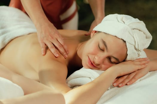 Beautiful young woman received a back massage on a spa bed from professional masseuse. Attractive female relaxes deeply by skilled hands of the massage therapist. Surrounded with nature. Tranquility.