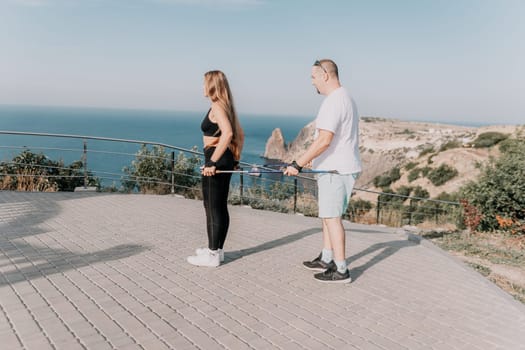 Happy Middle aged couple or friends practicing nordic walking in park near sea. Mature couple with trekking poles walking, practicing Nordic walking outdoors. Aging youthfully and sport concept.