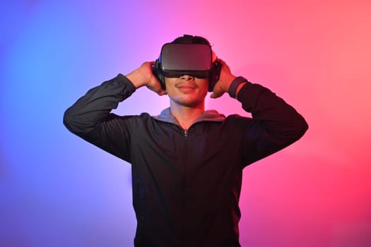 Young man wearing virtual reality headset standing over red and blue neon light.