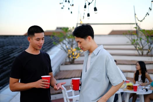 Happy young men chatting and drinking beer on a rooftop party. People lifestyle concept.