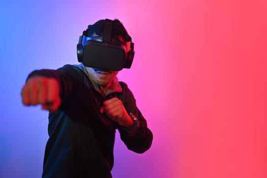 Young man having fun playing boxing game in VR glasses throwing punches in the air.