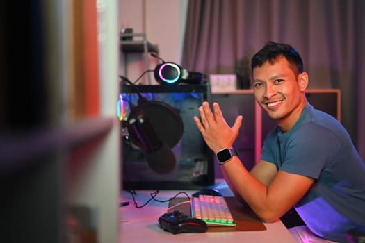 Portrait of handsome male gamer or streamer sitting at a table in a room with purple lights.