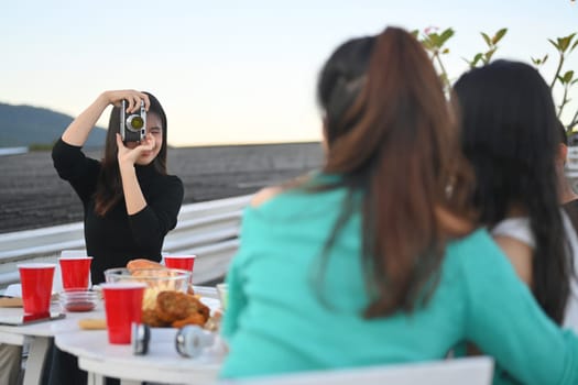 Young woman taking picture of friends having fun at party on rooftop during sunset.