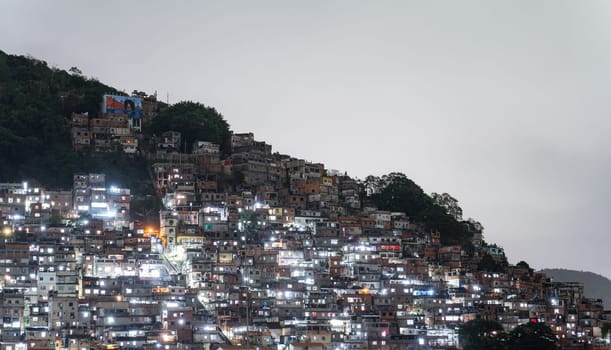 Brightly lit favela houses cover a hill in a Brazilian city, creating a vibrant nighttime scene.