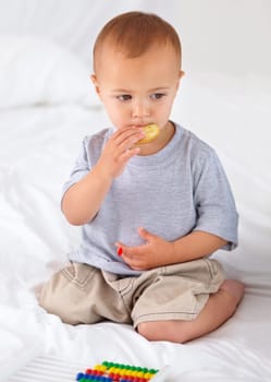 Cute, bed and baby eating biscuit for yummy snack playing with abacus for education. Child development, sweet and hungry young boy kid, infant or toddler enjoying a cracker in bedroom at home