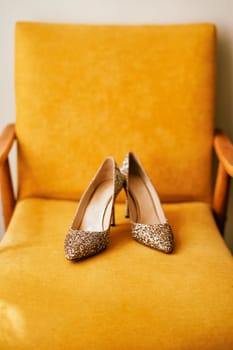 Bride shiny high-heeled shoes stand on a yellow armchair. High quality photo