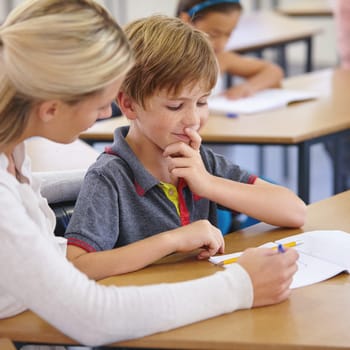 Teacher woman, boy and classroom with book, question and support for education with knowledge at desk. People, learning and child development with writing, advice and feedback with thinking at school.