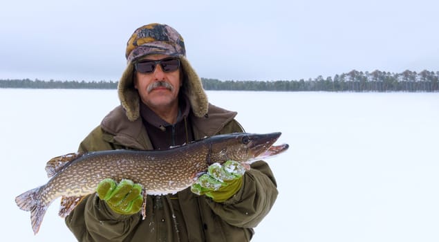 Man Holding a Fish in the Snow. Winter fishing, adventure. Banner, copy space