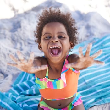 Excited, child and portrait on beach sand on towel, relax and summer holiday in sunshine in nature. Black, young girl or face by hand gesture on vacation, cape town or playing by ocean in outdoor.