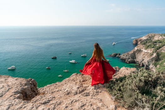 Woman sea red dress yachts. A beautiful woman in a red dress poses on a cliff overlooking the sea on a sunny day. Boats and yachts dot the background