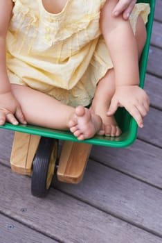 Baby, child and riding toy wagon in outdoors, plastic and fun activity for childhood. Kid, toddler and wheelbarrow for playing games on porch or deck, closeup and relaxing in construction equipment.