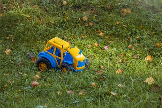 Children's toy yellow car forgotten on green grass, copy space