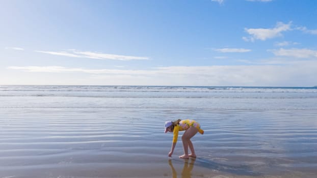 Little girl, braving the cold, joyfully runs in her swimsuit across the beach during winter.