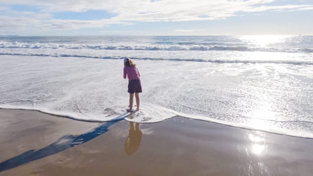 A little girl joyfully plays on the vast, empty sands of El Capitan State Beach in California during winter.