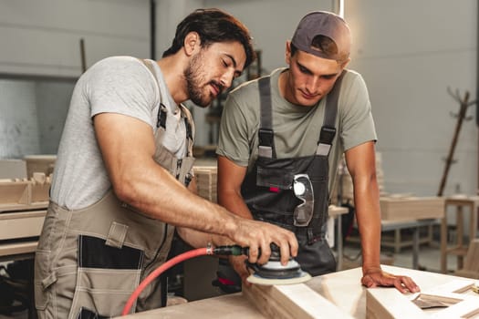 Two young carpenters working with wood standing at table in workshop close up