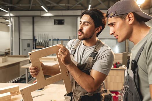 Two young men carpenters making furniture in warehouse of wood factory close up