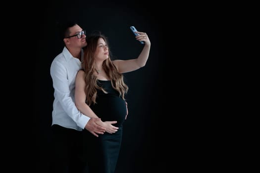 A young couple of parents-to-be taking selfies against at a black background