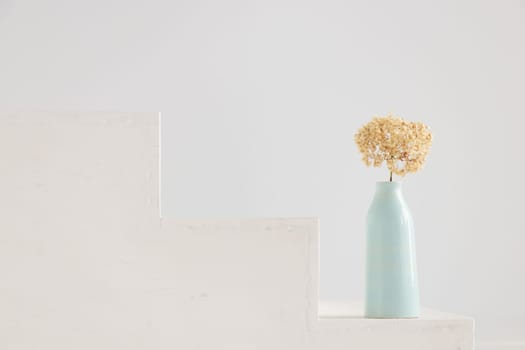 Dry hydrangea flower in blue vase on white house porch. Minimalist stilllife banner