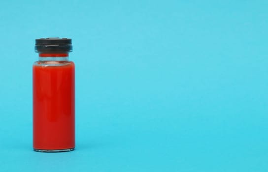 Ampoule with a blood test. Glass bottle with red liquid on a blue paper background.