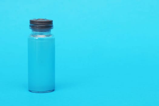 A bottle with a blue chemical reagent for research on a blue background. A glass ampoule with a rubber lid with a blue liquid on a blue paper background.
