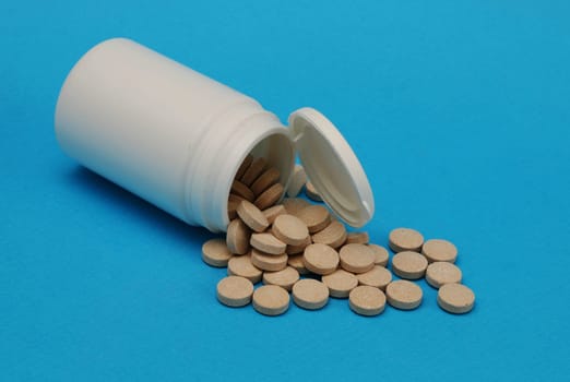 Pills spilled out from a white plastic bottle close-up. Medicine and health concept.