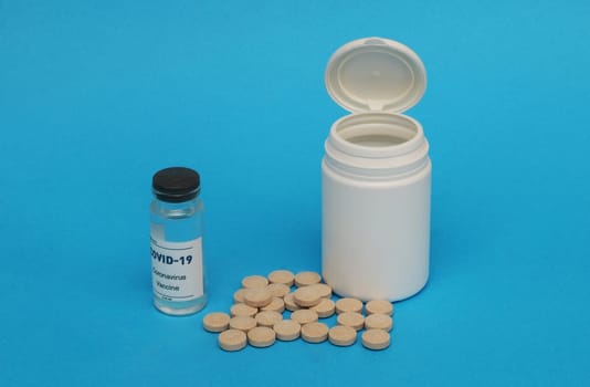 Plastic white bottle, brown pills, covid-19 vaccine ampoule on a blue background.