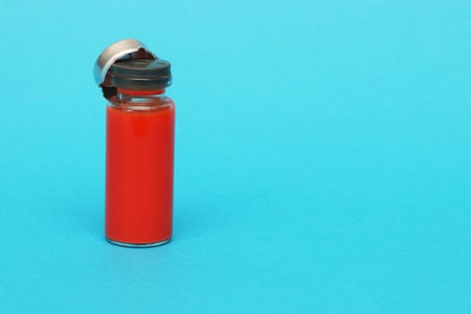 Glass medical bottle with a metal cap filled with blood. Glass bottle with red liquid on a blue paper background.