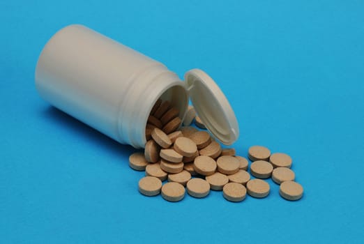 Pills spilled out from a white plastic bottle close-up.