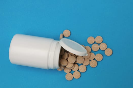 Close up of teblets pills spilling from Plastic pill bottle on blue background with selective focus. Medicine and health concept. Pills on a blue background top view.