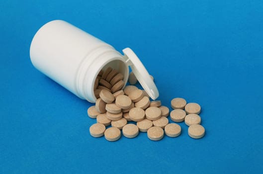 Pills spilled out from a white plastic bottle close-up.