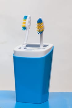 Two toothbrushes in a glass on a blue background close up