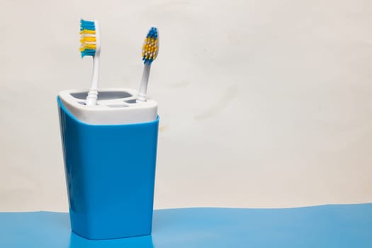 Two toothbrushes in a glass on a blue background, copy space