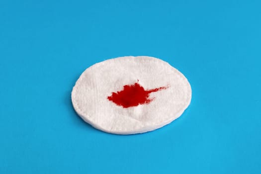Drop of blood on a cotton pad on a blue background close up