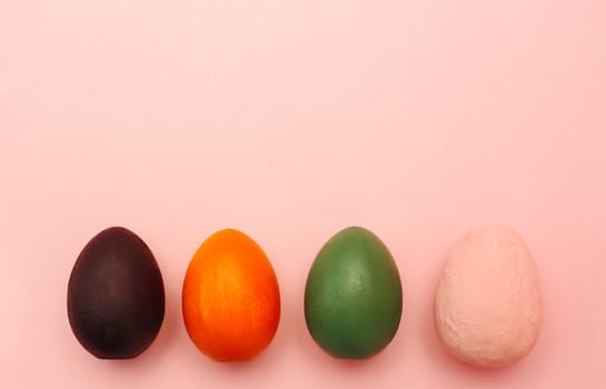 Brown, red, green, pink decorative eggs hand painted on a pastel pink background. concept of a holiday and a happy Easter.